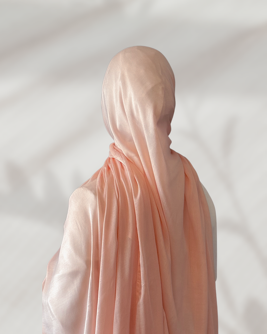 Person wearing a peach-colored hijab against a plain background